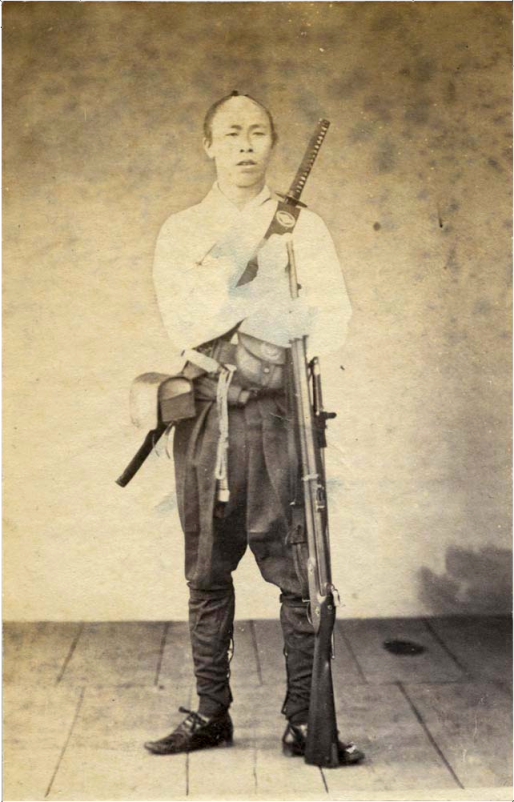 Japanese Samurai by Ueno Hikoma, 1860s. Note the modern European musket and larger sword bayonet that he carries in addition to a traditional sword worn across the back. Source: Wikimedia.