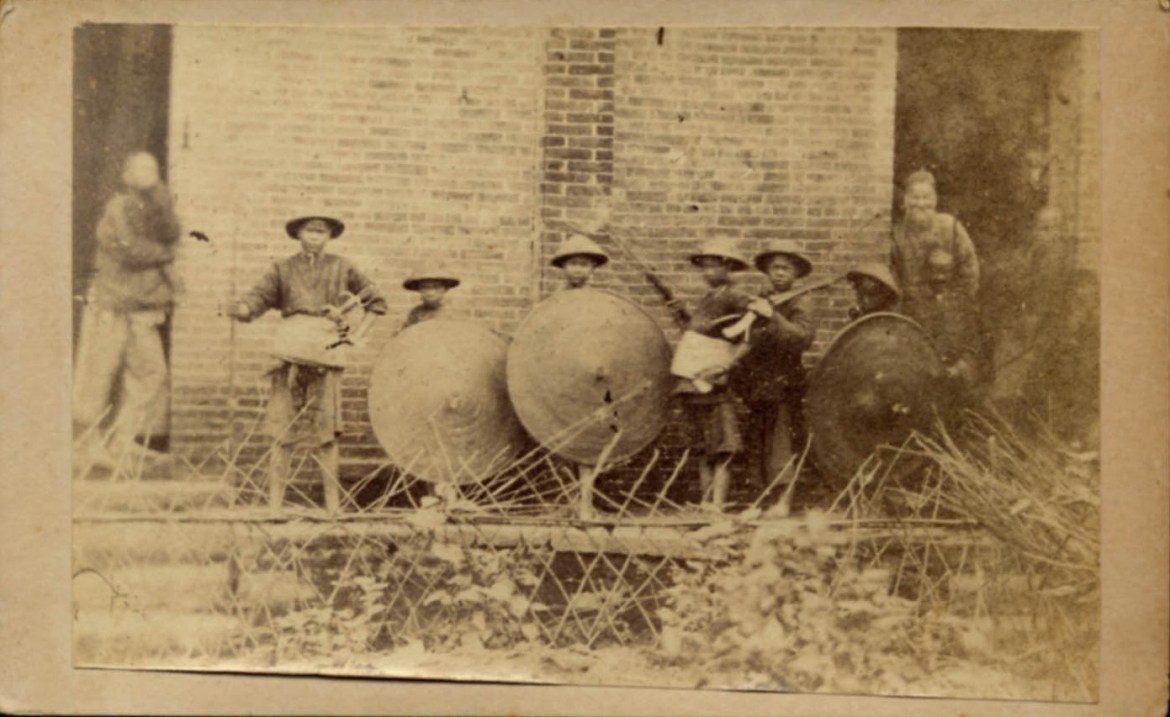 Another picture of the same young militia group, thistime in their home village. Luckily the hudiedao of the leader have become dislodged in their sheath. We can now confirm that these are double blades, and they are of the long, narrow stabbing variety seen in some of the prior photographs. Source http:\www.swordsantiqueweapons.com. 